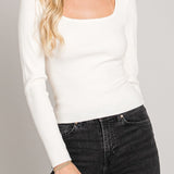 Woman wearing a white long-sleeve top and black jeans against a gray background