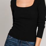 Woman wearing a black long-sleeve top and blue jeans on a gray background