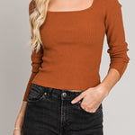 Woman wearing a brown ribbed sweater and black hat against a gray background