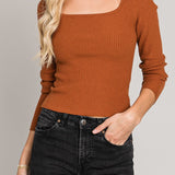 Woman wearing a brown ribbed sweater and black hat against a gray background