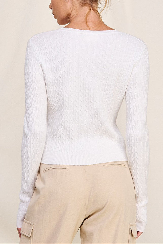 Woman wearing a white long-sleeve top and beige pants against a beige background