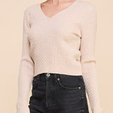 Woman wearing a beige sweater and black jeans against a beige background