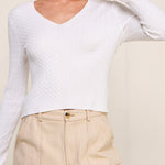 Woman wearing a white long-sleeve top and beige pants against a plain background