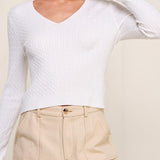 Woman wearing a white long-sleeve top and beige pants against a plain background