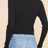 Woman wearing a black long-sleeve top and blue jeans on a beige background