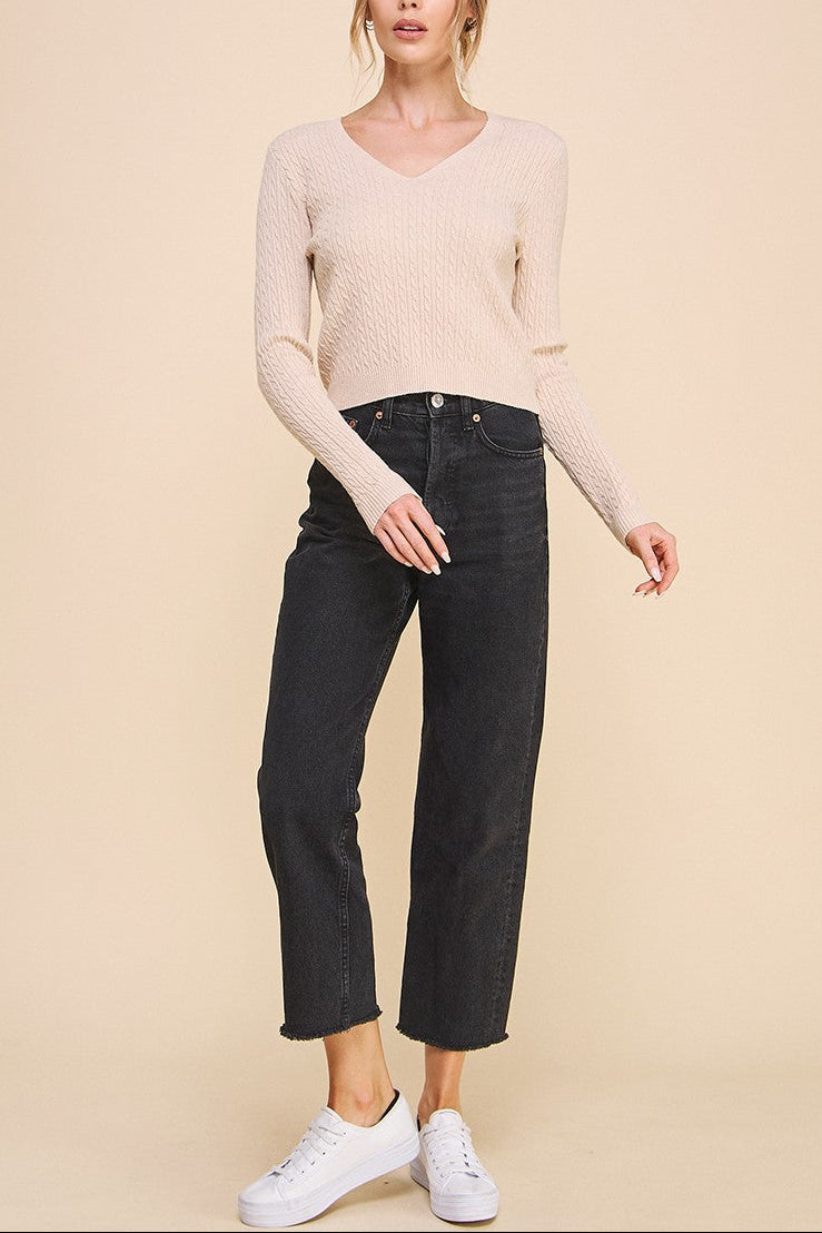 Woman wearing a beige sweater and black jeans against a beige background