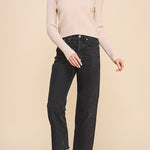 Woman wearing a beige sweater and black jeans against a beige background