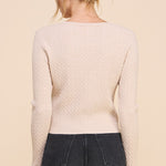 Person wearing a beige sweater and black pants against a beige background