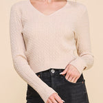 Woman wearing a beige cable knit sweater and black jeans on a beige background