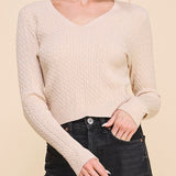 Woman wearing a beige cable knit sweater and black jeans on a beige background