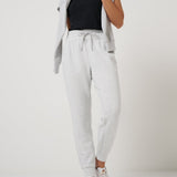 Woman wearing a black top, light gray cardigan, white pants, and white sneakers on a white background