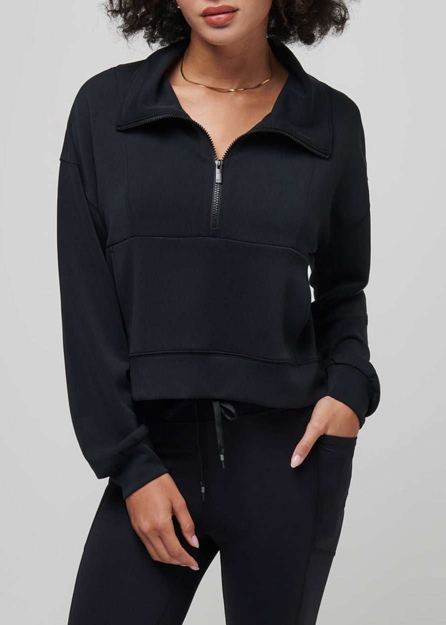 Woman wearing a black half-zip sweatshirt against a gray background