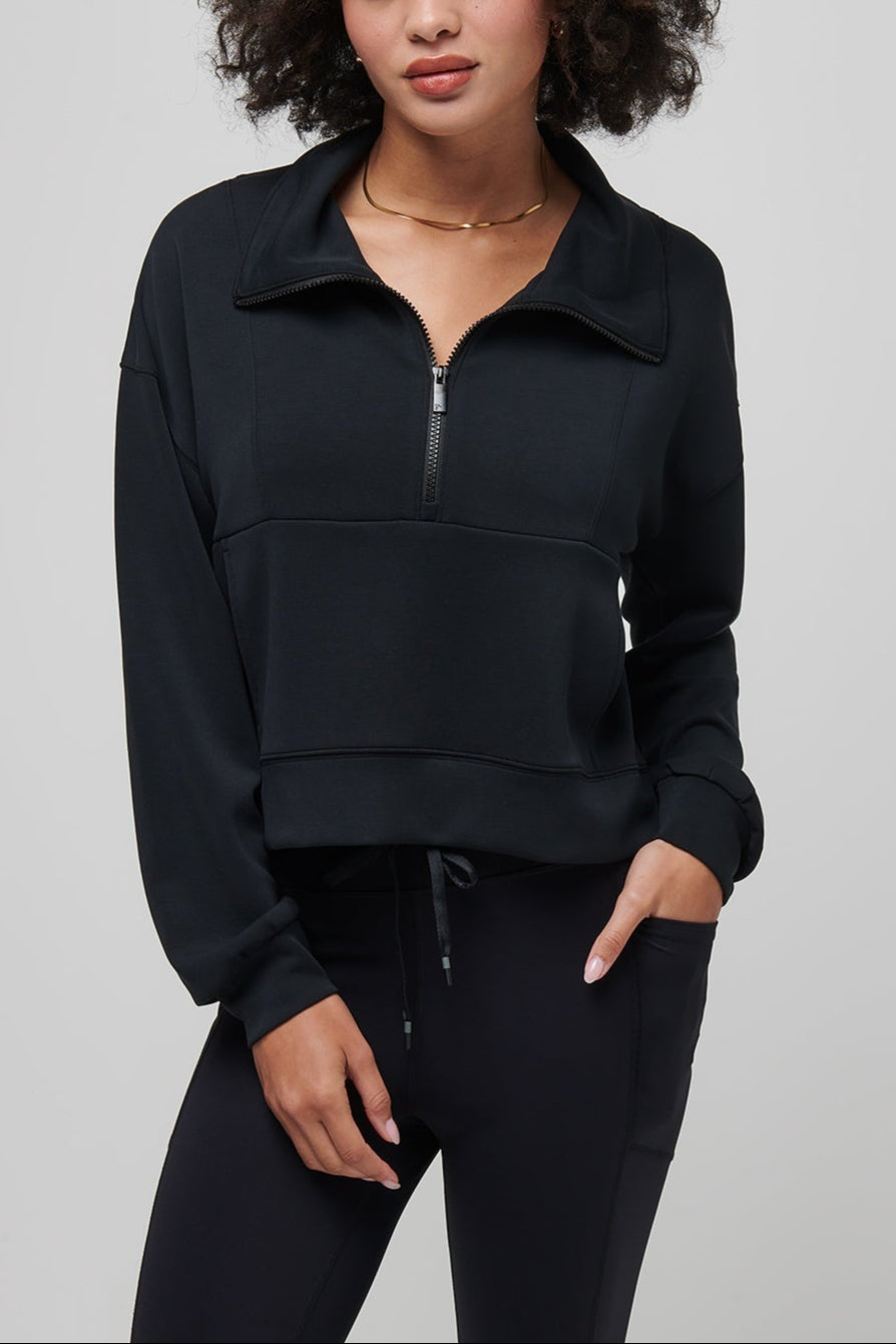 Woman wearing a black half-zip sweatshirt against a gray background
