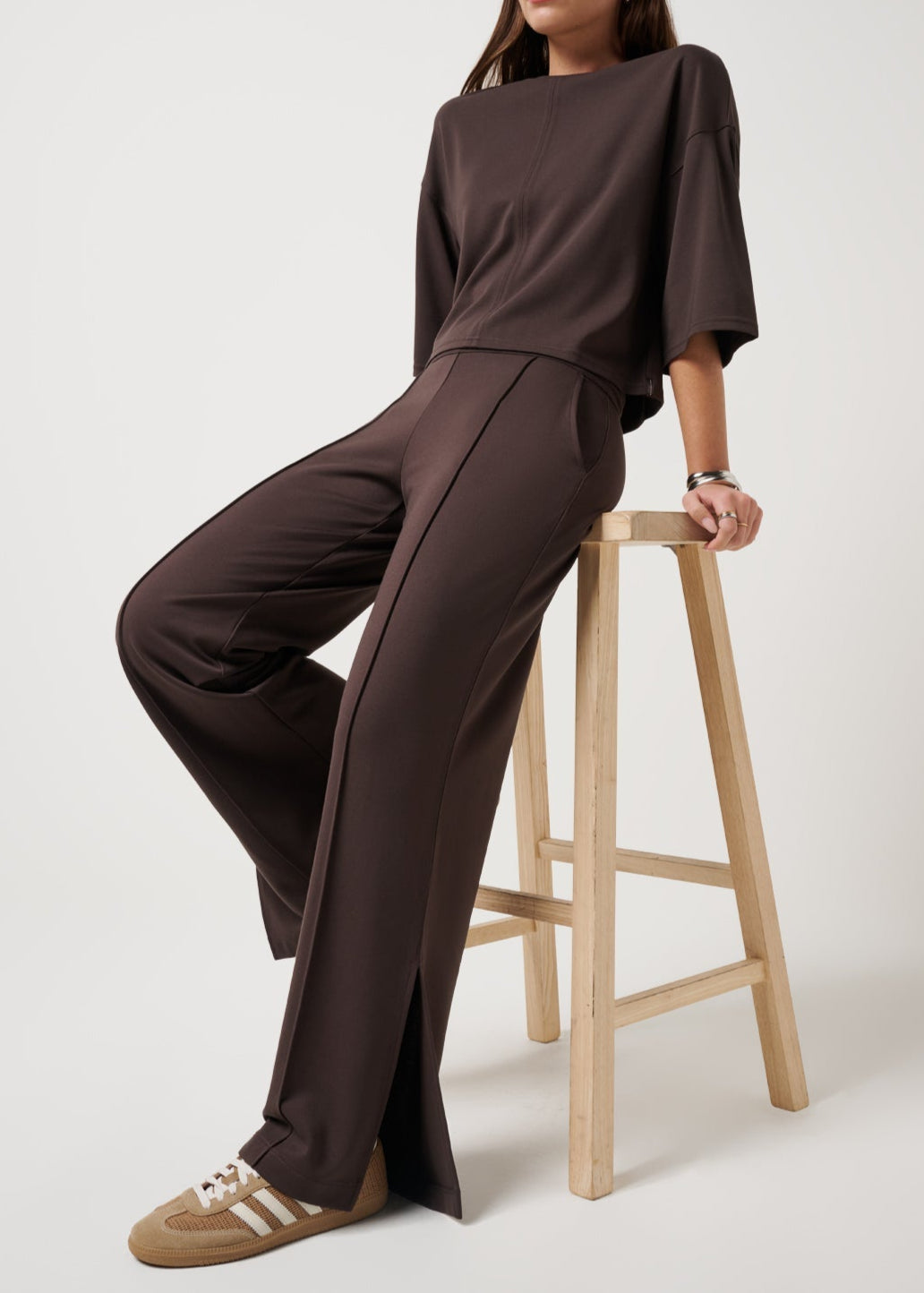 Woman wearing a brown outfit sitting on a wooden stool against a white background