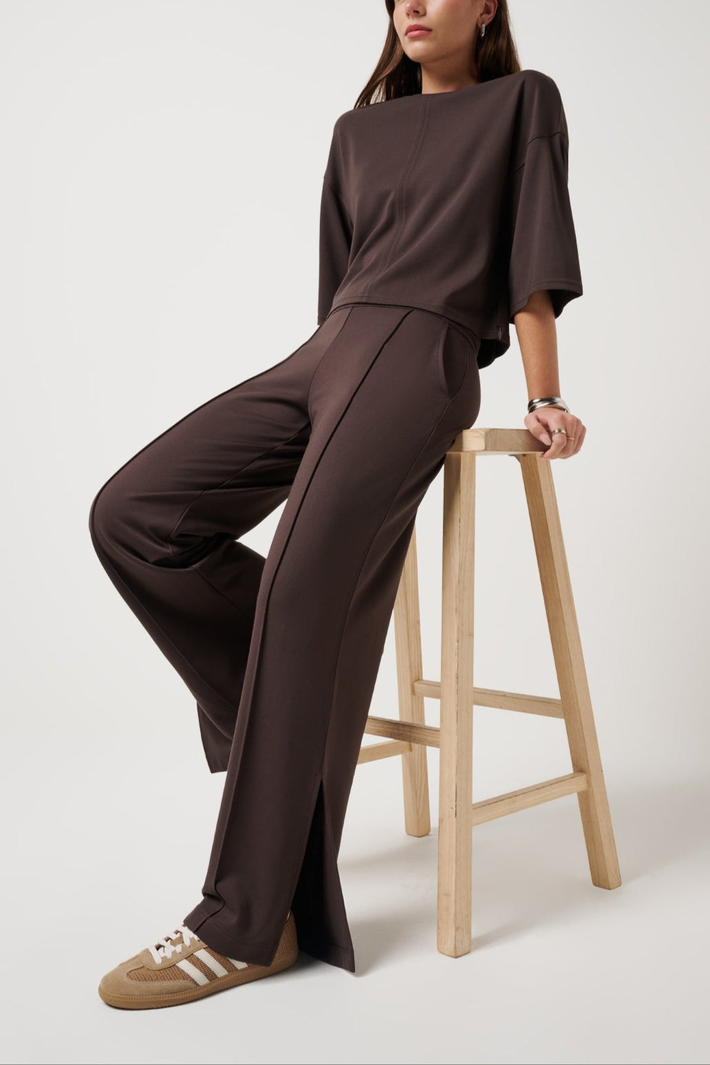 Woman wearing a brown outfit sitting on a wooden stool against a white background