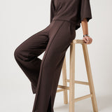 Woman wearing a brown outfit sitting on a wooden stool against a white background