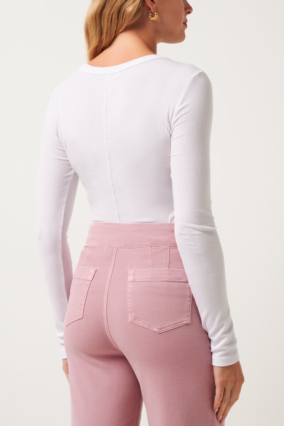 Woman wearing a white long-sleeve top and pink pants on a white background