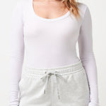 Woman wearing a white long-sleeve top and light gray shorts on a white background