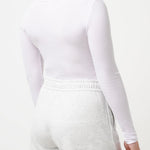 Woman wearing a white long-sleeve top and shorts on a light gray background