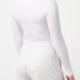 Woman wearing a white long-sleeve top and shorts on a light gray background
