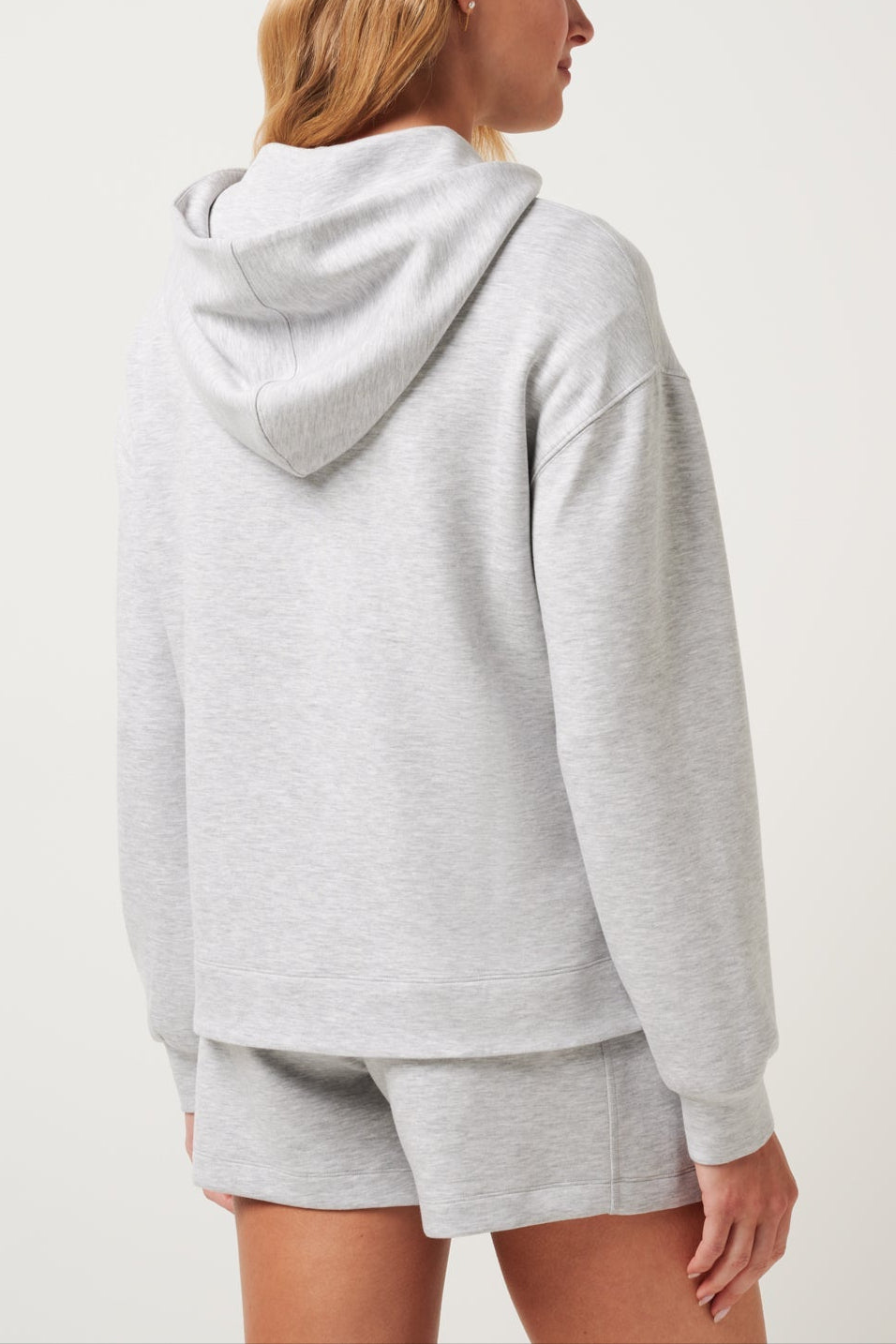 Person wearing a gray hoodie and shorts set on a white background