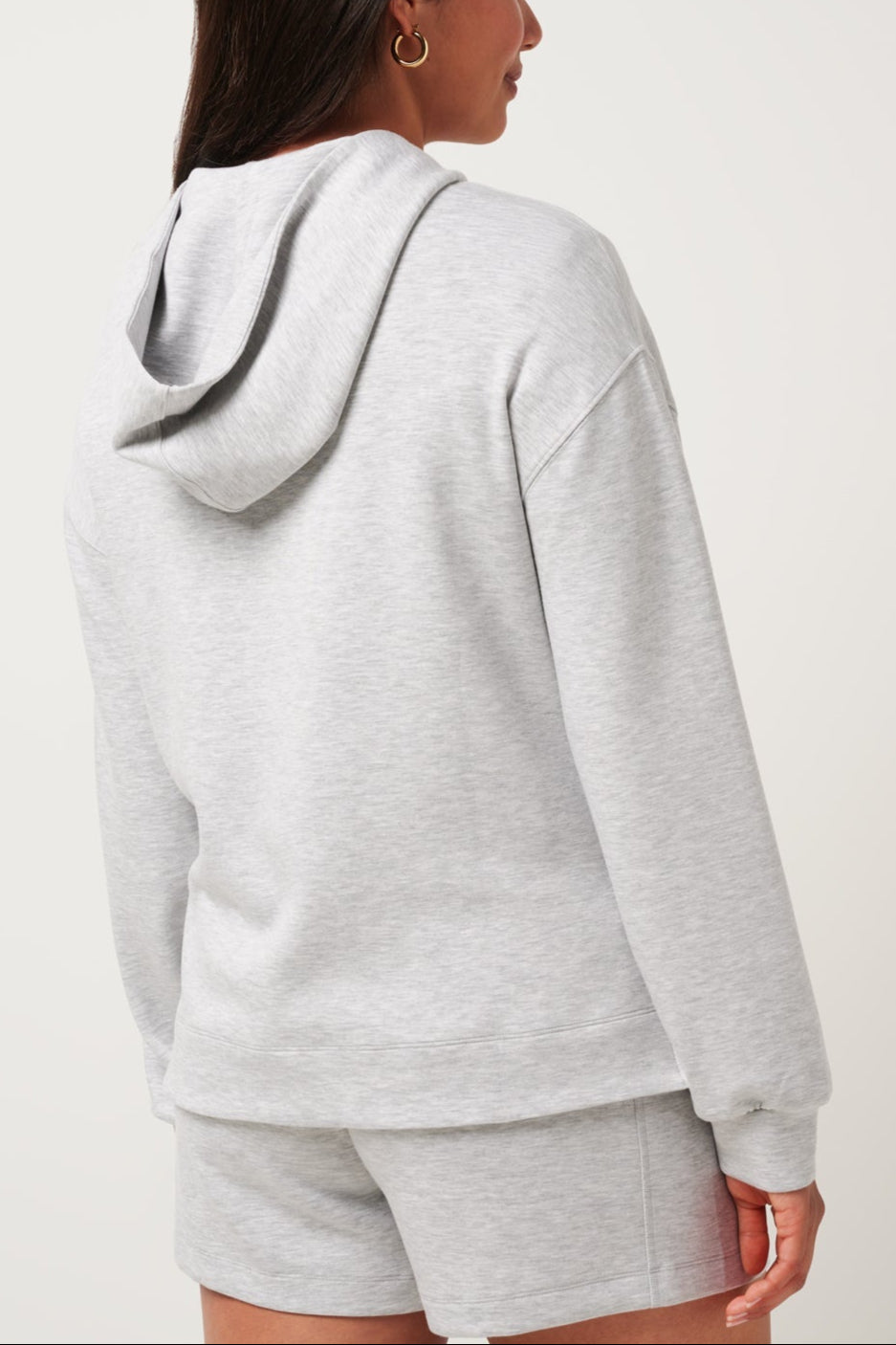 Person wearing a gray hoodie and shorts set on a white background