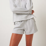 Woman wearing a gray hoodie and shorts set on a plain background