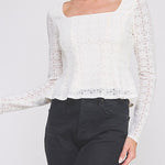 Woman wearing a white lace blouse and black pants on a plain background