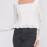 Woman wearing a white lace blouse and black pants on a plain background