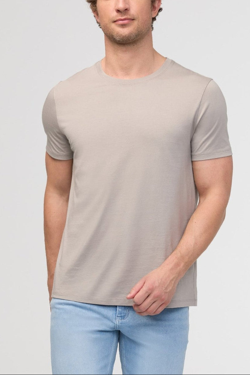 Man wearing a beige t-shirt and light blue jeans against a plain background