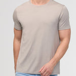 Man wearing a beige t-shirt and light blue jeans against a plain background