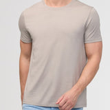 Man wearing a beige t-shirt and light blue jeans against a plain background