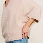 Woman wearing a beige sweater and blue jeans against a plain background