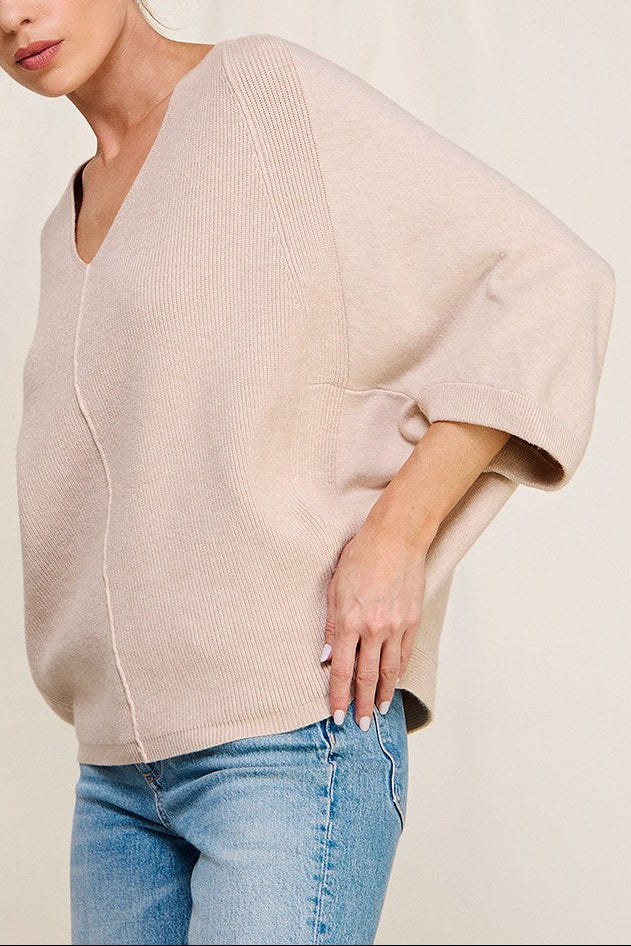 Woman wearing a beige sweater and blue jeans against a plain background