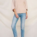 Woman wearing a beige sweater and light blue jeans on a plain background