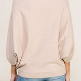 Woman wearing a beige sweater and blue jeans on a plain background