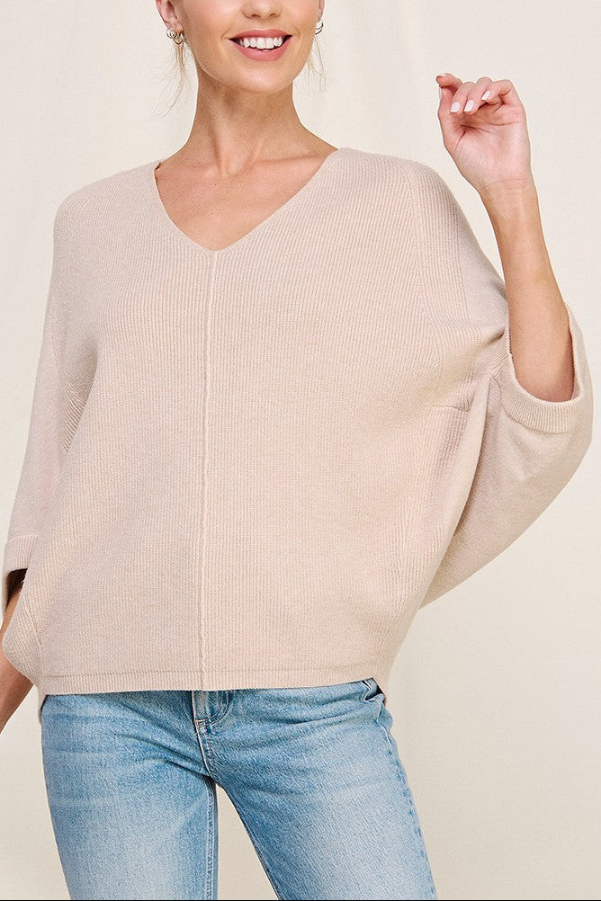 Woman wearing a beige sweater and blue jeans against a plain background