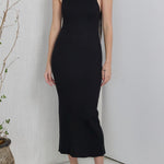 Woman wearing a black dress standing in a minimalistic room with a plant.