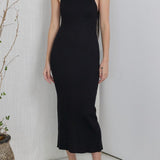 Woman wearing a black dress standing in a minimalistic room with a plant.