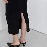 Person wearing a black ribbed dress with a high slit on a white background