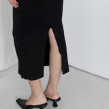 Person wearing a black ribbed dress with a high slit on a white background