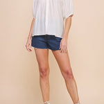 Woman wearing a white blouse and denim shorts on a beige background