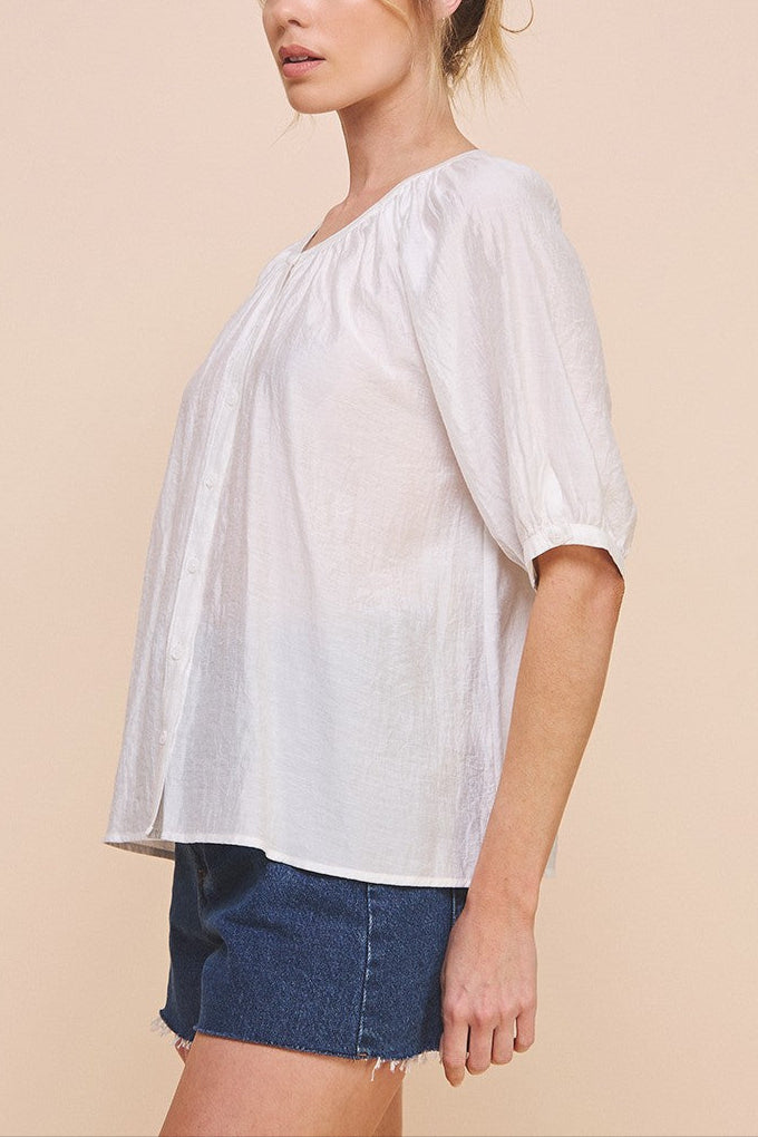 Woman wearing a white blouse with a gradient effect and denim shorts on a beige background