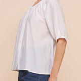 Woman wearing a white blouse with a gradient effect and denim shorts on a beige background