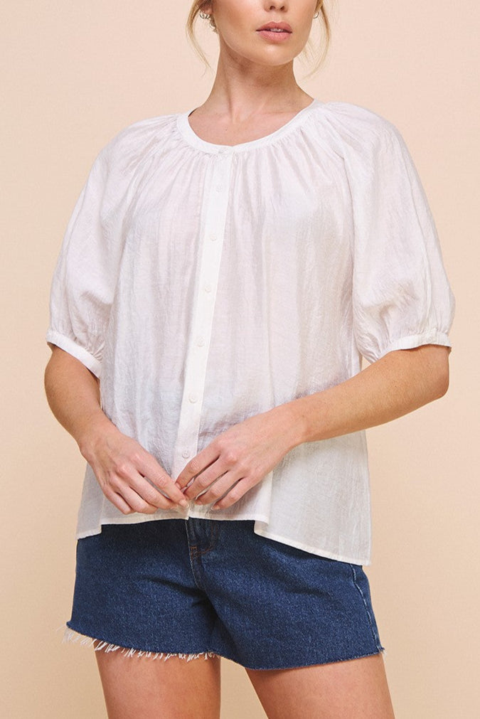 Woman wearing a white blouse and denim shorts against a beige background