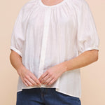 Woman wearing a white blouse and denim shorts against a beige background