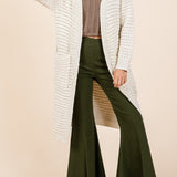 Woman wearing a long white cardigan, brown top, and green pants on a beige background