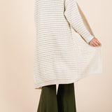 Woman wearing a long cream cardigan over green pants on a beige background