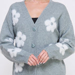 Woman wearing a gray cardigan with white floral patterns on a plain background