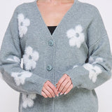 Woman wearing a gray cardigan with white floral patterns on a plain background